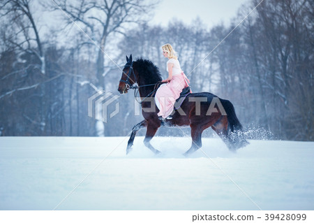 Young woman in dress riding horse on winter field 39428099