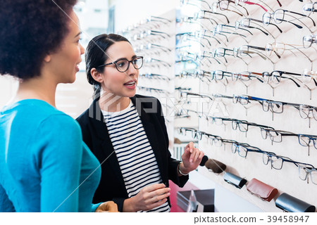 Black woman inspecting glasses in optician shelf Black woman inspecting glasses in optician shelf 39458947