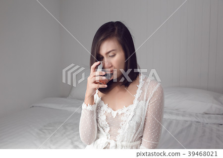 Asian woman in white nightgown drinking water on the bed at bedr 39468021
