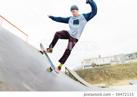 A skateboarder teenager in a hat does a trick with 39472115