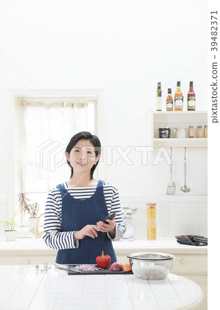 觀看一個智能手機的婦女在廚房裡 觀看一個智能手機的婦女在廚房裡 39482371