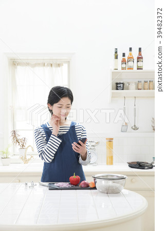 觀看一個智能手機的婦女在廚房裡 觀看一個智能手機的婦女在廚房裡 39482372