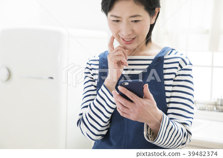 觀看一個智能手機的婦女在廚房裡 觀看一個智能手機的婦女在廚房裡 39482374