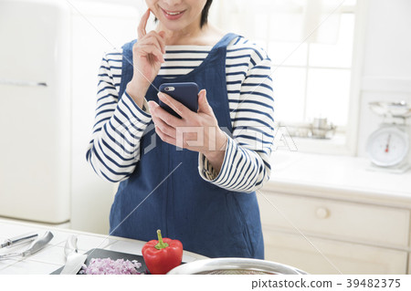 A woman watching a smartphone in the kitchen A woman watching a smartphone in the kitchen 39482375