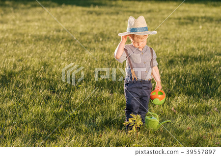 Toddler child outdoors. One year old baby boy wearing straw hat using watering can Toddler child outdoors. One year old baby boy wearing straw hat using watering can 39557897