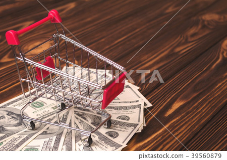 Empty shopping trolley on a pile of dollars on a wooden background 39560879