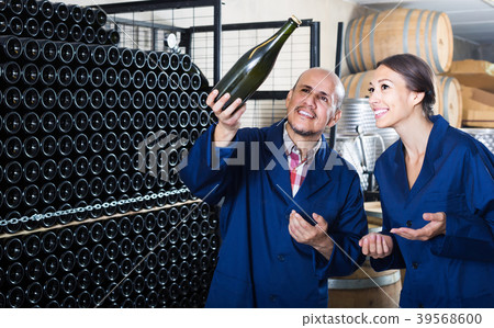 man and women coworkers looking at bubbly wine in bottle standing in wine cellar 39568600