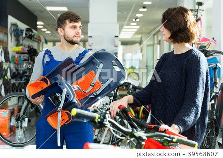 Portrait of man seller showing kids bicycle chair to woman Portrait of man seller showing kids bicycle chair to woman 39568607