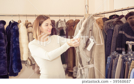 Cheerful woman customer examining sheepskin coat 39568687