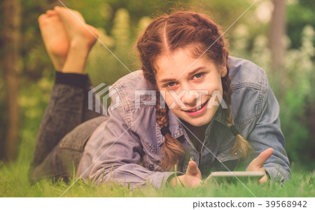 smiling young female using digital tablet while lying in outdoors 39568942