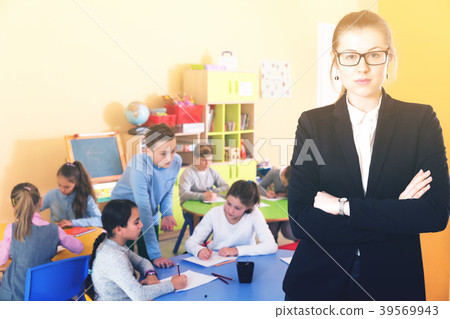 Strict female teacher standing foreground in classroom Strict female teacher standing foreground in classroom 39569943