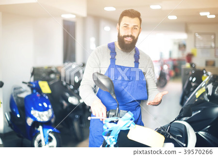friendly man worker displaying various motorcycles in workshop friendly man worker displaying various motorcycles in workshop 39570266