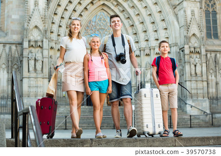 Traveling family of four strolling with luggage along European city street 39570738