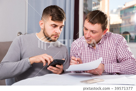 Serious males with documents and phone at home table Serious males with documents and phone at home table 39571377