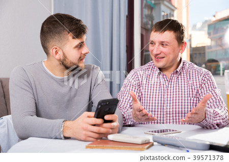 Happy male friends using phone at home table Happy male friends using phone at home table 39571378