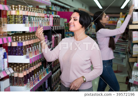 woman picking scented spray from shelf in cosmetics store 39572196