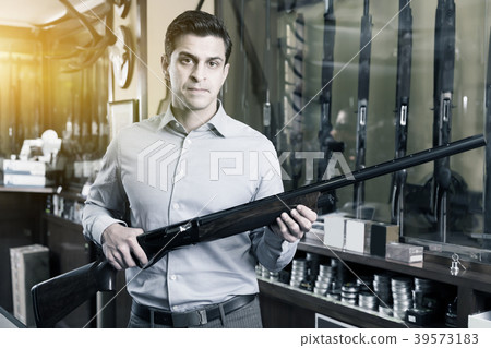 Happy male hunter choosing shotgun in store Happy male hunter choosing shotgun in store 39573183