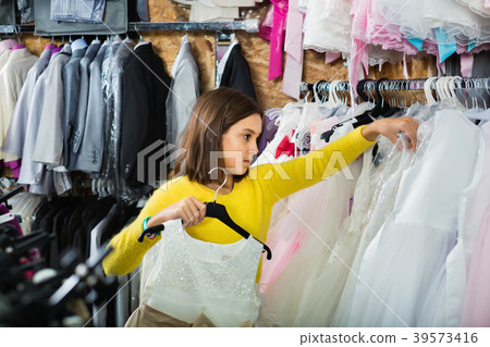 Teenage customer examining dresses in children’s cloths shop 39573416