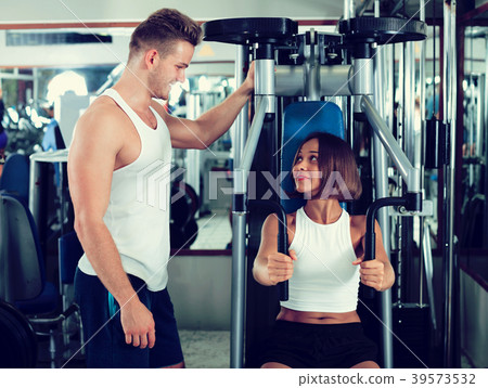Man coach assisting woman in using pec deck Man coach assisting woman in using pec deck 39573532