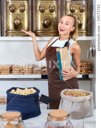 Portrait of girl seller who is standing near showcase with nuts in alimentacion store. 39573781