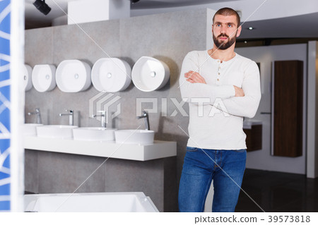 Positive young man buyer standing near bathroom fitment Positive young man buyer standing near bathroom fitment 39573818