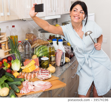 Cheerful woman is taking selfie by phone in time cooking on the kitchen Cheerful woman is taking selfie by phone in time cooking on the kitchen 39574196