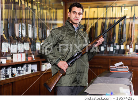 Hunter male wearing windbreaker in hunting shop with rifle in hands 39574283