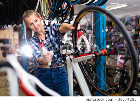 Young female is cheking wheels of bicycle in workshop. Young female is cheking wheels of bicycle in workshop. 39574285