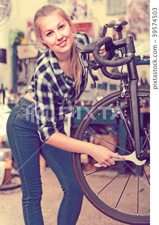 Female is fixing wheels of bicycle in workshop. 39574503
