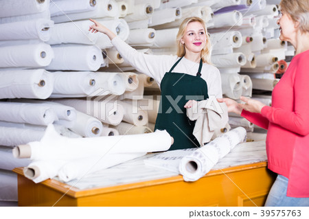 young female seller demonstrating fabrics to senior buyer in textile shop 39575763