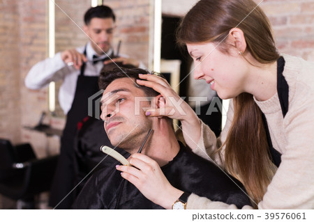 Woman barber shaving client with straight razor Woman barber shaving client with straight razor 39576061