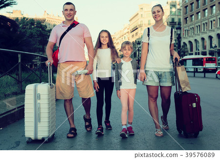 traveling family of four strolling with luggage along European city street traveling family of four strolling with luggage along European city street 39576089