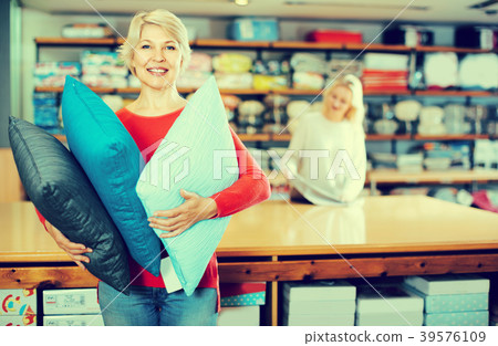 Smiling senior seller is showing wide assortment of pillows Smiling senior seller is showing wide assortment of pillows 39576109