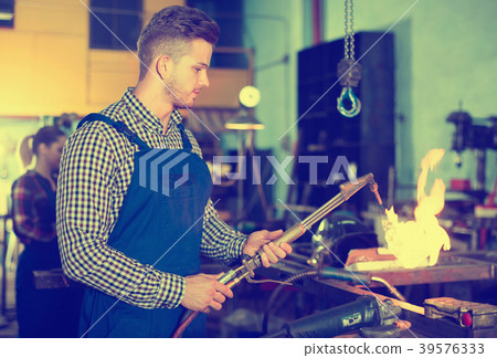 Portrait of master who is working with burner in protection in workshop. Portrait of master who is working with burner in protection in workshop. 39576333