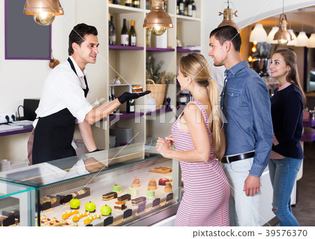 Young seller helping friends to choose sweets Young seller helping friends to choose sweets 39576370