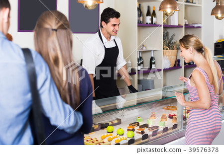Young seller helping clients to choose sweets Young seller helping clients to choose sweets 39576378