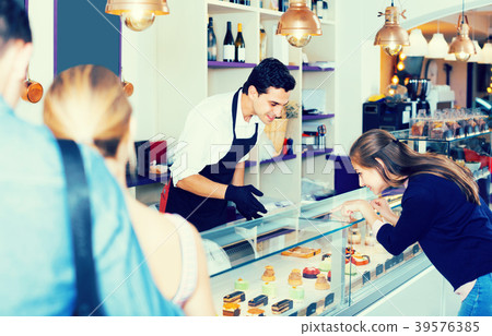 Friends are choosing delicious cakes from showcase 39576385