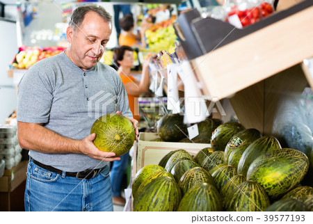 Smiling male is choosing green melon in the supermarket. 39577193