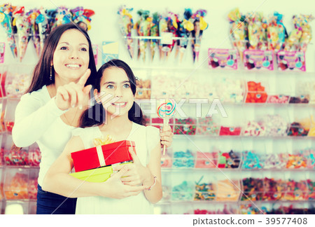 Smiling girl with gifts and female point finger in candy store Smiling girl with gifts and female point finger in candy store 39577408