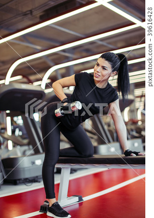 woman flexing muscles with dumbbell on bench in woman flexing muscles with dumbbell on bench in 39616428