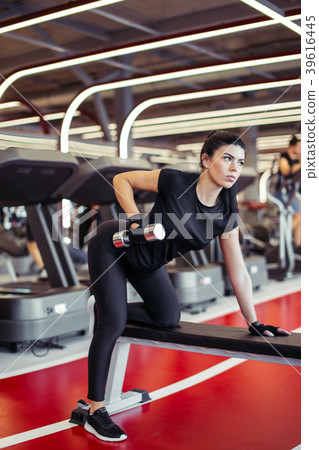 woman flexing muscles with dumbbell on bench in woman flexing muscles with dumbbell on bench in 39616445