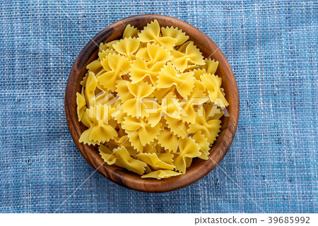 farfalle macaroni pasta in a wooden bowl on a blue farfalle macaroni pasta in a wooden bowl on a blue 39685992