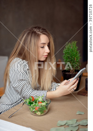 Young woman sitting at the table looks at phone Young woman sitting at the table looks at phone 39710716