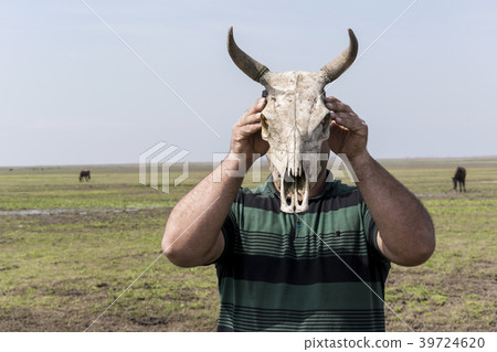 Young man holding a cow skull in front of his head Young man holding a cow skull in front of his head 39724620