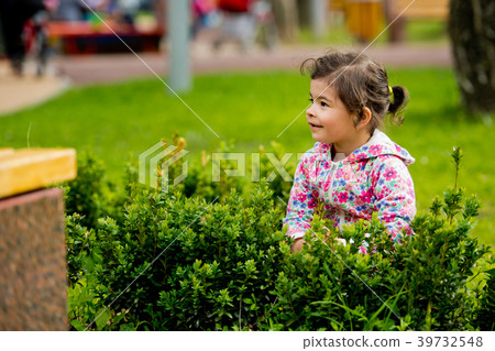 Little cute girl sitting in green bush. 39732548