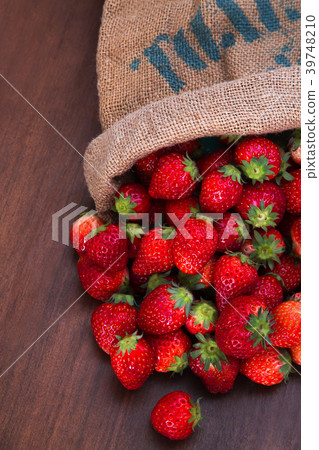 Many fresh strawberries overflowing from a hemp bag 39748210