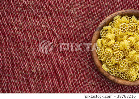 Macaroni ruote pasta in a wooden bowl on a red Macaroni ruote pasta in a wooden bowl on a red 39768210