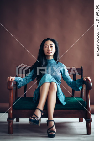 Confident asian girl in blue dress sits on sofa Confident asian girl in blue dress sits on sofa 39790560