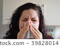 Woman blowing her nose hard into a tissue at home 39828014