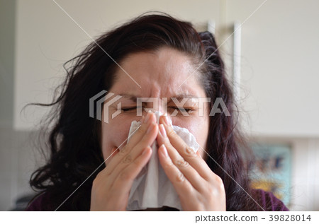 Woman blowing her nose hard into a tissue at home 39828014